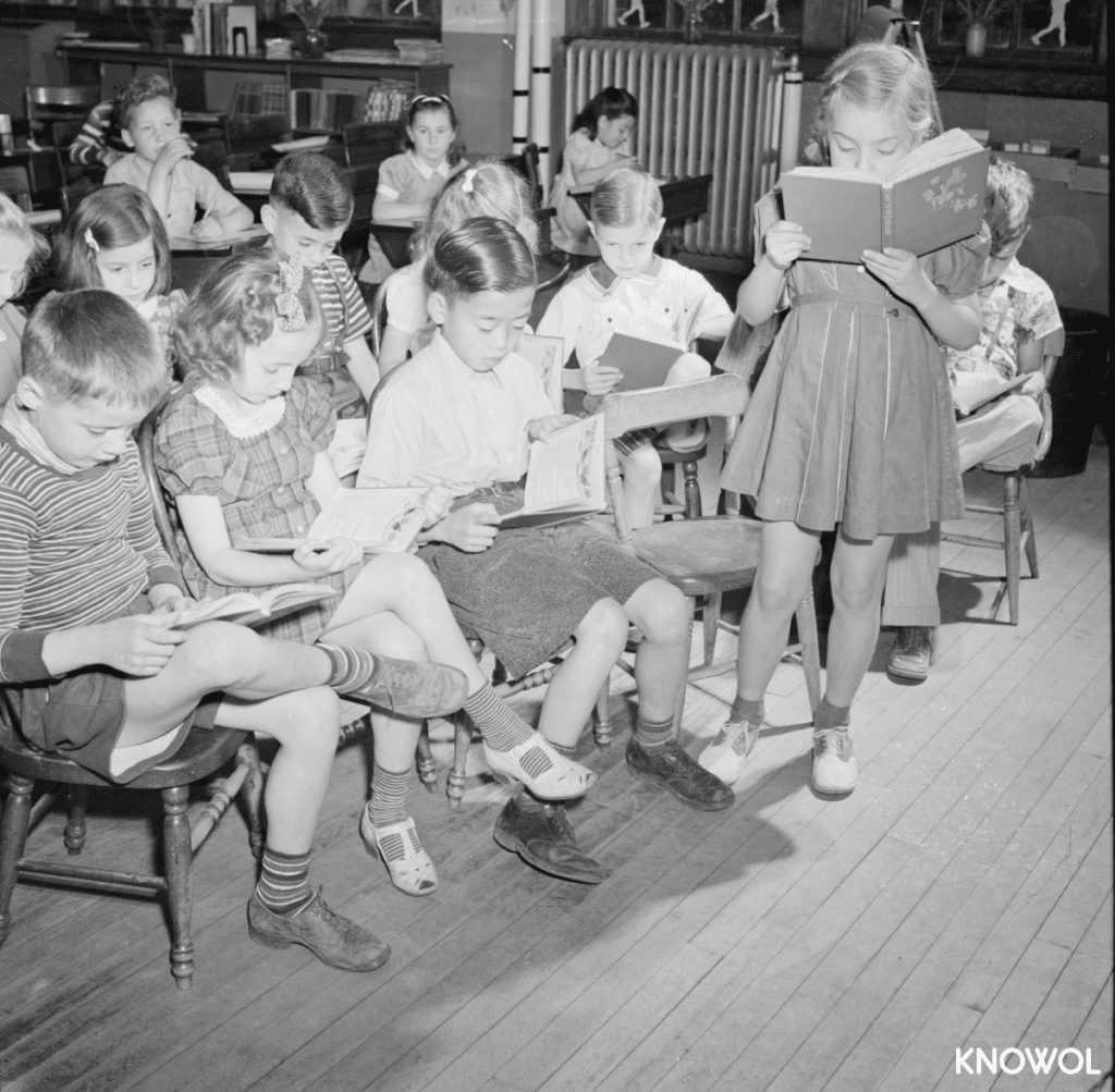A young girl reading a book out loud to the class.