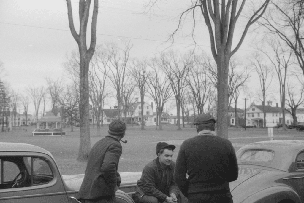 A group of three men sitting on a car and smoking a pipe near the Colchester Town Green in November, 1940.