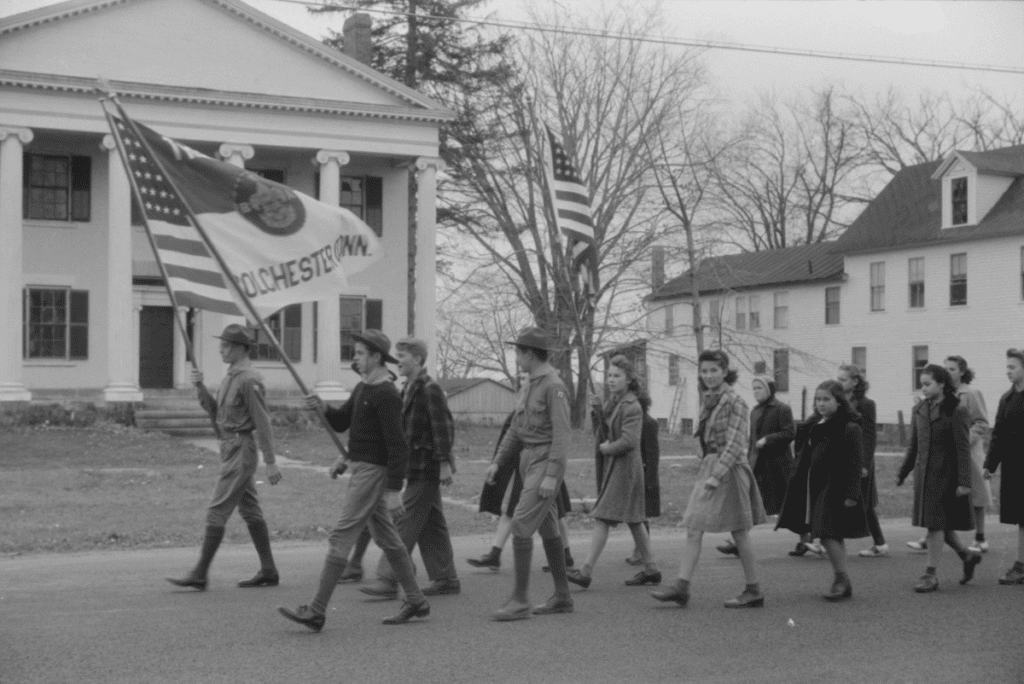This picture shows local boy scouts marching in the Armistice Day parade with an American Flag and a Colchester, Connecticut