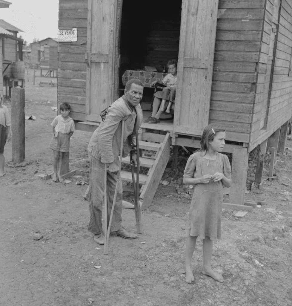 A disabled man and children stand in front of this house that reads "Se Vende", meaning "For Sale".
