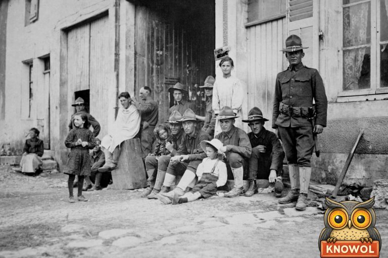 American soldiers in campaign hats sit with children outside a house in a French village while one soldier gets a haircut