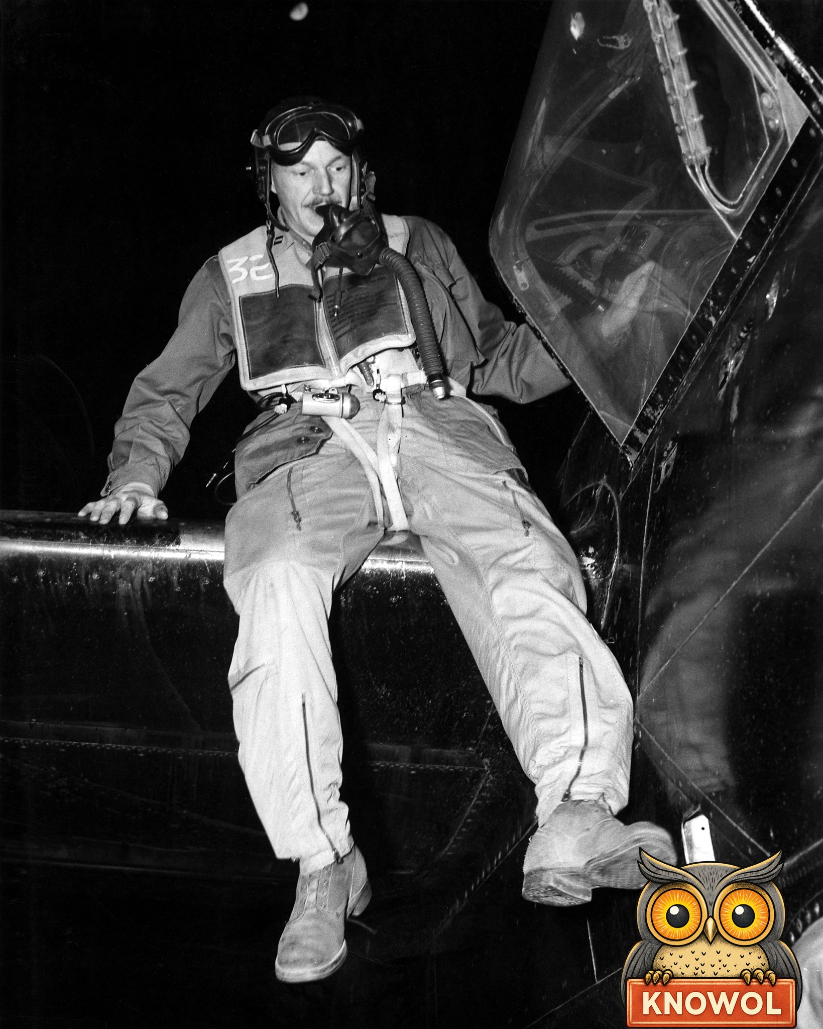 Capt. Donald R. DeFoe in a flying helmet, goggles and life vest, with his oxygen mask at his mouth, climbs out of the open canopy of his black B-26 bomber at night