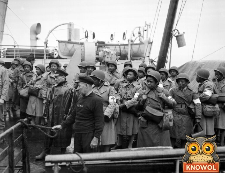 U.S. Army nurses in steel helmets and raincoats, many with red cross armbands, line a ship's rail at Greenock, Scotland, 1944