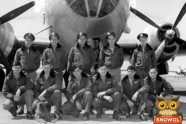 Eleven American airmen in fur-collared flight jackets pose in two rows in front of the glass nose of a B-29 bomber, with a dog lying at their feet