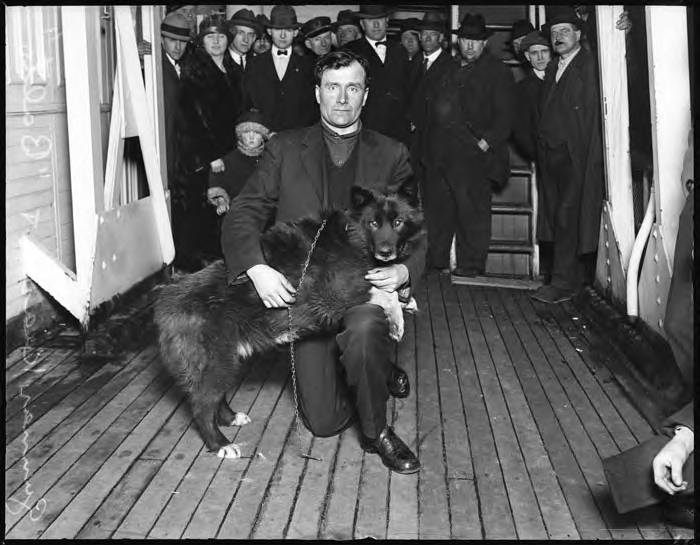 1925 photo of musher Gunnar Kaasen kneeling beside his lead dog Balto, a dark husky, in Seattle