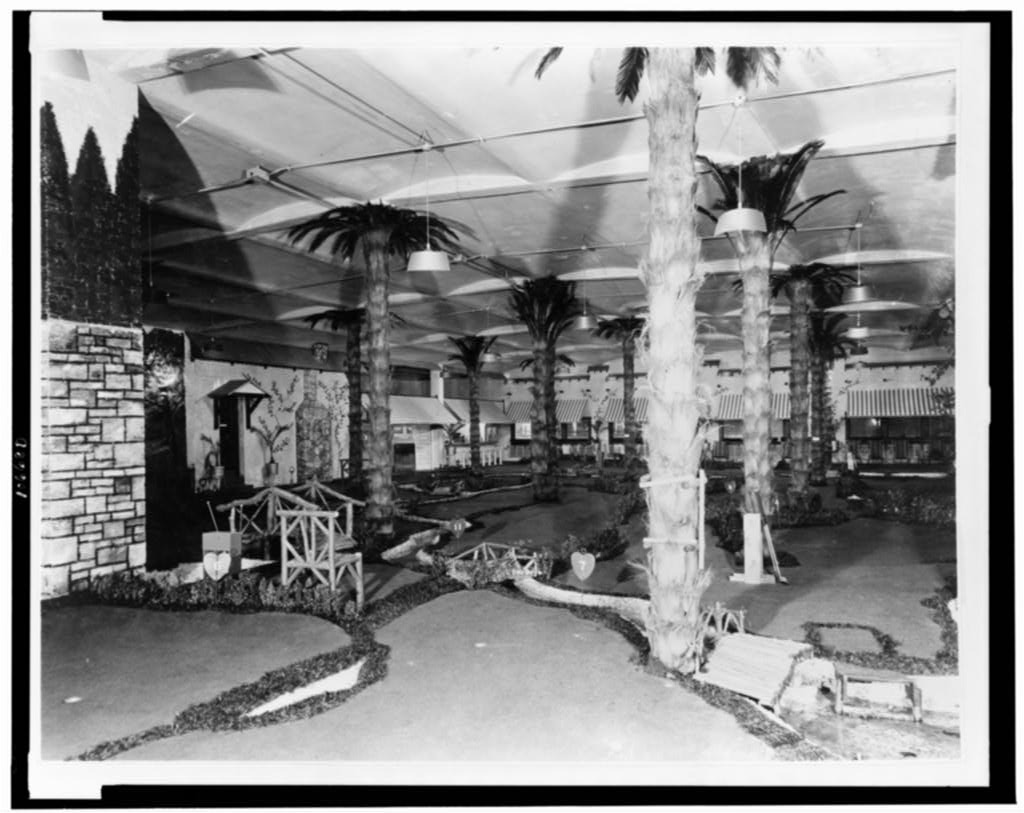 An indoor miniature golf course in Chicago around 1930, with artificial palm trees, rustic wooden bridges and hanging lamps